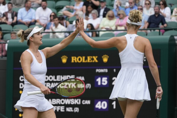 CORRECTS SPELLING OF LAST NAME TO ROUTLIFFE, NOT ROUTINE AS ORIGINALLY SENT - Gabriela Dabrowski of Canada, left, with playing partner Erin Routliffe of New Zealand, touch hands after winning a point as they play against Caroline Dolehide of the United States and Desirae Krawczyk of the United States during their semifinal doubles match at the Wimbledon tennis championships in London, Friday, July 12, 2024.(AP Photo/Alastair Grant)