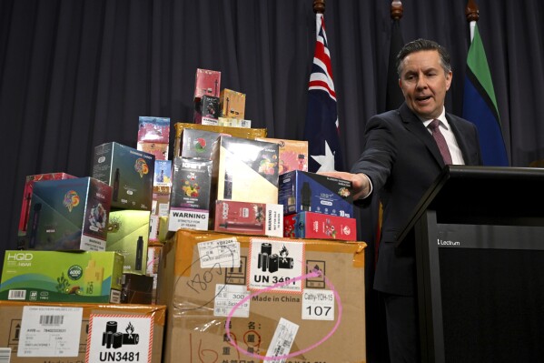 Australian Health Minister Mark Butler speaks gestures towards boxes of electronic cigarettes during a press conference at Parliament House in Canberra, Australia, Wednesday, Feb. 28, 2024. Australia announced plans, Monday, June 24, to outlaw the sale of vapes outside pharmacies from next week under some of the world's toughest restrictions on electronic cigarettes. (Lukas Coch/AAP Image via AP)
