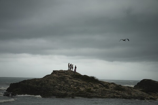 People stand on a rock during the aftermath of Hurricane Beryl in Tulum, Mexico, July 5, 2024. (AP Photo/Fernando Llano)