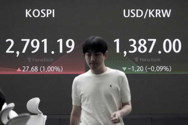 A currency trader passes by the screen showing the Korea Composite Stock Price Index (KOSPI), left, and the foreign exchange rate between U.S. dollar and South Korean won at the foreign exchange dealing room of the KEB Hana Bank headquarters in Seoul, South Korea, Tuesday, July 23, 2024. (AP Photo/Ahn Young-joon)