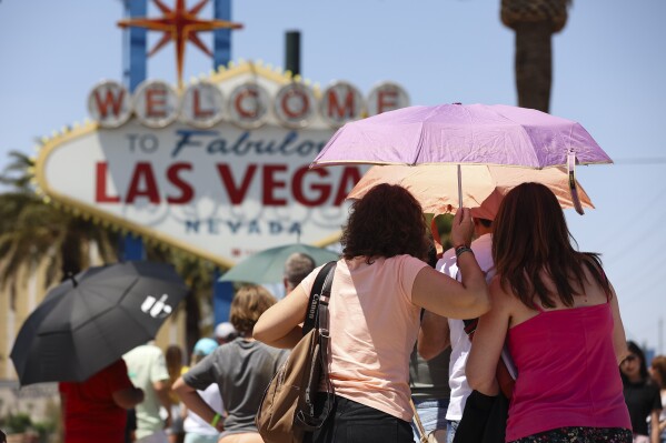 FILE - People use umbrellas to block the sun while waiting to take a photo at the "Welcome to Las Vegas" sign July 8, 2024, in Las Vegas. (Wade Vandervort/Las Vegas Sun via AP)