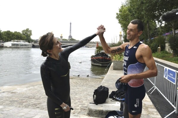 In this photo provided by the Ministry Of Sport, Olympic And Paraolympic Games, France's Minister of Sports and the Olympic and Paralympic Games Amelie Oudea-Castera, left and Tokyo 2020 Paralympics Triathlon gold medalist Alexis Hanquinquant gesture ahead of swimming in the River Seine, in Paris, Saturday, July 13, 2024. Oudéa-Castéra took a symbolic dip in the Seine on Saturday, less than two weeks before the start of the Paris 2024 Olympic Games. (Ministry Of Sport, Olympic And Paraolympic Games via AP)