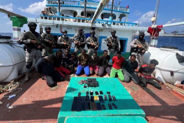 This photograph provided by the Indian Navy shows armed naval commandos standing behind 10 captured Somali pirates with their hands tied behind after they thwarted a piracy attempt on the Iranian flagged fishing vessel Al Naeemi off the east coast of Somalia, Monday, Jan.29, 2024. According to a navy statement Tuesday, Indian naval ship Sumitra intercepted the vessel and freed its 19-member Pakistani crew. The navy did not immediately say what had happened to the pirates. (Indian Navy via AP)