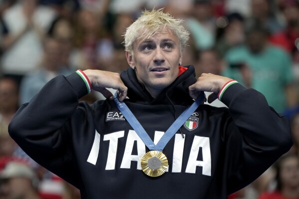 Gold medalist Nicolo Martinenghi reacts on the podium after winning the men's 100-meter breaststroke final at the 2024 Summer Olympics, Sunday, July 28, 2024, in Nanterre, France. (AP Photo/Matthias Schrader)