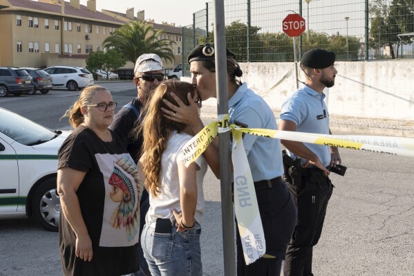 A police officer kisses a girl outside a school following a stabbing attack in Azambuja near Lisbon, Tuesday, Sept. 17, 2024. (AP Photo/Ana Brigida)