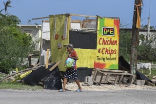 A woman walks past a food stall destroyed by Hurricane Beryl in the fishing settlement of Rocky Point, Clarendon, Jamaica, Thursday, July 4, 2024. (AP Photo/Collin Reid)