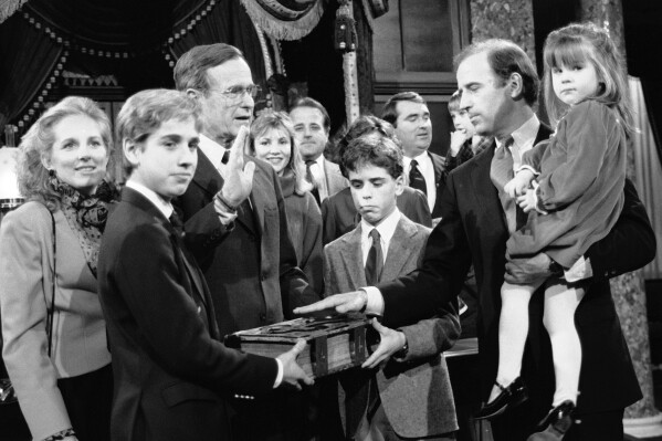 FILE - Sen. Joe Biden, D-Del., holds his daughter Ashley while taking a mock oath of office from Vice President George Bush during a ceremony, Jan. 3, 1985, on Capitol Hill, in Washington. Biden's sons Beau and Hunt hold the bible during the ceremony. Historians and political advisers say history will be kinder to President Joe Biden than voters have been. Biden dropped out of the presidential race Sunday, July 21, 2024, clearing the way for a new Democratic nominee. (AP Photo/Lana Harris, File)