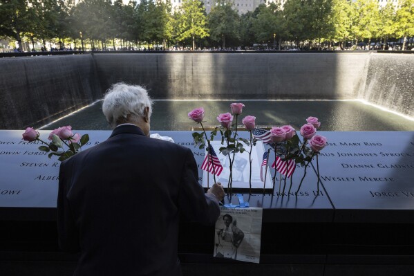 Hagi Abucar places flowers for his former coworker Lindsey Herkness on the south reflecting pool during the 9/11 Memorial ceremony on the 23rd anniversary of the Sept. 11, 2001 attacks, Wednesday, Sept. 11, 2024, in New York. (AP Photo/Yuki Iwamura)