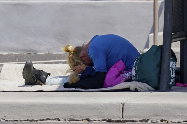 FILE - With hands covering their forehead, a person waits at a bus stop as temperatures are expected to hit 116 degrees on July 18, 2023, in Phoenix. (AP Photo/Ross D. Franklin, File)