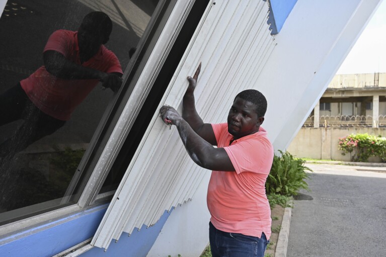 A man covers the windows of a building to protect it from the incoming Hurricane Beryl in Kingston, Jamaica, Tuesday, July 2, 2024. (AP Photo/Collin Reid)