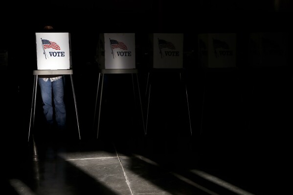 FILE - Voting booths are illuminated by a shaft of sunlight as people cast their ballots at a polling site in Billings, Mont., on Nov. 6, 2012. (AP Photo/Jae C. Hong, File)