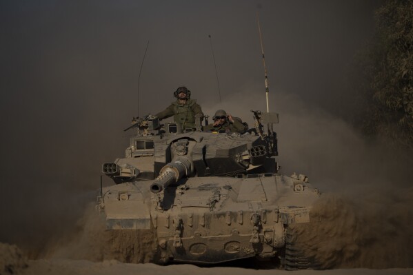 Israeli soldiers move on the top of a tank near the Israeli-Gaza border, as seen from southern Israel, Monday, July 8, 2024. Israeli forces advanced deeper into the Gaza Strip's largest city in pursuit of militants who had regrouped there, sending thousands of Palestinians fleeing on Monday from an area ravaged in the early weeks of the nine-month-long war. (AP Photo/Leo Correa)