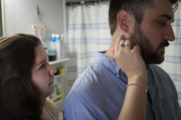 Julia Manetta applies an anti-nausea patch on the neck of her husband, Steven, a cancer patient, Thursday, Aug. 29, 2024, in their Lemont, Ill., home. (AP Photo/Charles Rex Arbogast)