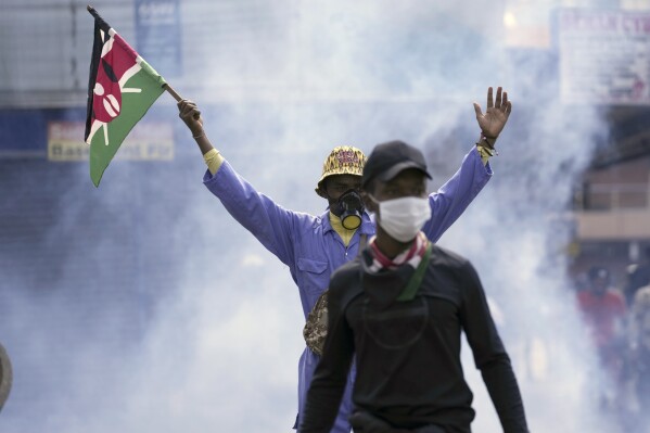 An anti-government protester waves a Kenyan flag as police fire tear gas at them during a protest over proposed tax hikes in a finance bill in downtown Nairobi, Kenya Tuesday, June. 25, 2024. (AP Photo/Brian Inganga)