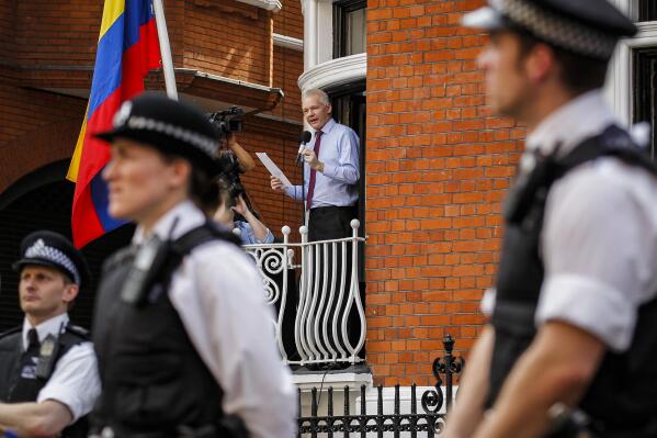 FILE - British police stand guard as WikiLeaks founder Julian Assange, center, address media and supporters from a window of the Ecuadorian Embassy in central London, Aug. 19, 2012. Two lawyers and two journalists are suing the CIA, saying the agency obtained copies of the contents of their electronic devices and helped enable the recording of their meetings with Assange, during the latter part of his seven-year stay at the embassy. The plaintiffs seek compensatory and punitive damages in a lawsuit filed Monday, Aug. 15, 2022 in Manhattan federal court.(AP Photo/Sang Tan, File)