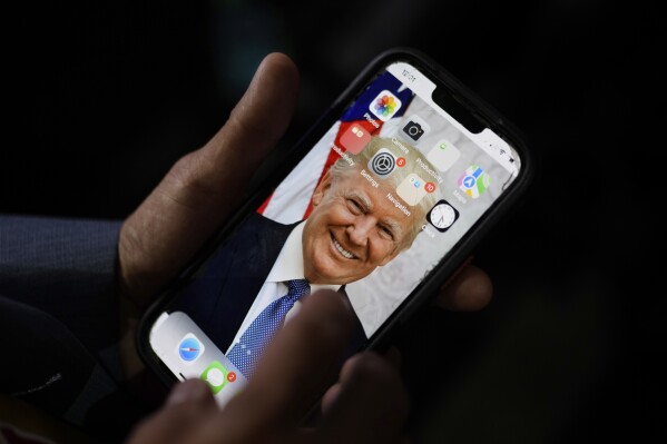 California delegate T. Tran holds his phone with an image of Republican presidential candidate former President Donald Trump as he waits before the Republican National Convention Wednesday, July 17, 2024, in Milwaukee. (AP Photo/Jae C. Hong)