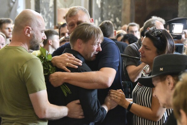 Friends hug Yaroslav Bazylevych during the funeral service for his family in the Garrison Church in Lviv, Ukraine, Friday, Sept. 6, 2024. Bazylevych's wife Yevgenia and their three daughters - Darina, 18, Emilia, 7, and Yaryna, 21 - were killed in Wednesday's Russian missile attack. (AP Photo/Mykola Tys)