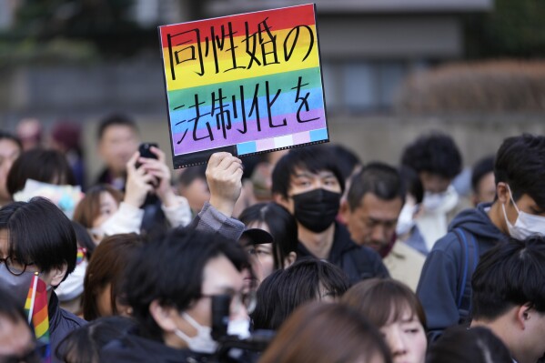 FILE - A supporter for the LGBTQ+ community holds up a poster as plaintiffs speak in front of media members by the main entrance of the Tokyo district court after hearing the ruling regarding LGBTQ+ marriage rights, in Tokyo, on March 14, 2024. The poster reads, "Legalize the same-sex marriage." A Japanese high court has approved a legal gender change for a transgender woman without requiring the usual compulsory gender-affirming surgery. The Hiroshima High Court ruled Wednesday July 10, 2024 that the current requirement is possibly unconstitutional, signalling a change in how gender issues and LGBTQ+ rightgs are being addressed in Japan. (AP Photo/Hiro Komae, File)