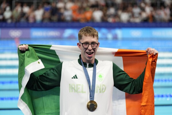 Gold medalist Daniel Wiffen, of Ireland, poses for a photo with his national flag on the podium following the men's 800-meter freestyle final at the 2024 Summer Olympics, Tuesday, July 30, 2024, in Nanterre, France. (AP Photo/Ashley Landis)