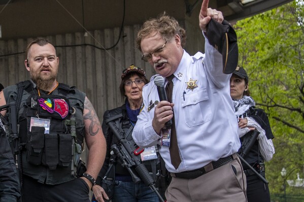 FILE - Barry County Sheriff Dar Leaf, front right, speaks next to members of the Michigan Liberty Militia during the "American Patriot Rally-Sheriffs speak out" event at Rosa Parks Circle in downtown Grand Rapids, Mich., Monday, May 18, 2020. Leaf, who has attempted to cast doubt on the results of the 2020 presidential election through multiple investigations, is running for reelection against other Republicans. (Cory Morse/The Grand Rapids Press via AP, File)