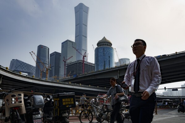 Pedestrians cross an intersection with the background of the central business district in Beijing, China, Monday, July 15, 2024. China's ruling Communist Party is starting a four-day meeting Monday that is expected to lay out a strategy for self-sufficient economic growth in an era of heightened national security concerns and restrictions on access to American technology. (AP Photo/Vincent Thian)