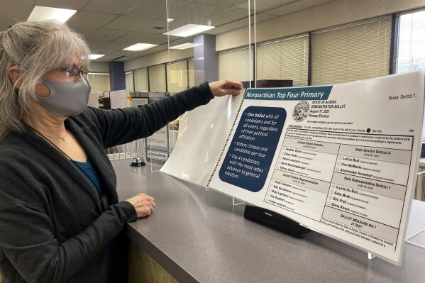 FILE - Deborah Moody, an administrative clerk at the Alaska Division of Elections office in Anchorage, Alaska, looks at an oversized booklet explaining election changes in the state on Jan. 21, 2022. A state court judge has disqualified a number of booklets used to gather signatures for an initiative that aims to repeal Alaska's ranked choice voting system.(AP Photo/Mark Thiessen, File)