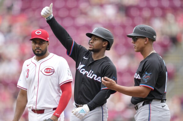Miami Marlins' Xavier Edwards, center, gestures after hitting a single as Cincinnati Reds first baseman Jeimer Candelario looks on during the sixth inning of a baseball game, Sunday, July 14, 2024, in Cincinnati. (AP Photo/Jeff Dean)