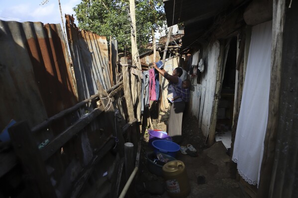 Jacinter Awino, 33, carries her son as she does laundry in the Kibera slum of the capital Nairobi, Kenya, Tuesday, May 28, 2024. Jacinter shares a small tin house with her husband and four children. The 33-year-old housewife and her mason husband are unable to raise the $3,800 purchase price for a one-room government house. Their tin one was constructed for $380 and lacks a toilet and running water. (AP Photo/Andrew Kasuku)
