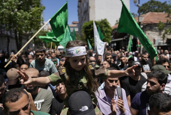 A Palestinian man carries a girl with a Hamas group headband that reads "the Qassam Brigades" while others fly Hamas flags, as they protest the assassination of Hamas top leader Ismail Haniyeh, in the West Bank city of Ramallah, Wednesday, July 31, 2024. Haniyeh was assassinated in Tehran, Iran's paramilitary Revolutionary Guard said early Wednesday. (AP Photo/Nasser Nasser)