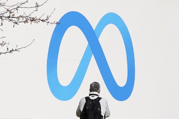 FILE - A person stands in front of a Meta sign outside of the company's headquarters in Menlo Park, Calif., March 7, 2023. (AP Photo/Jeff Chiu, File)