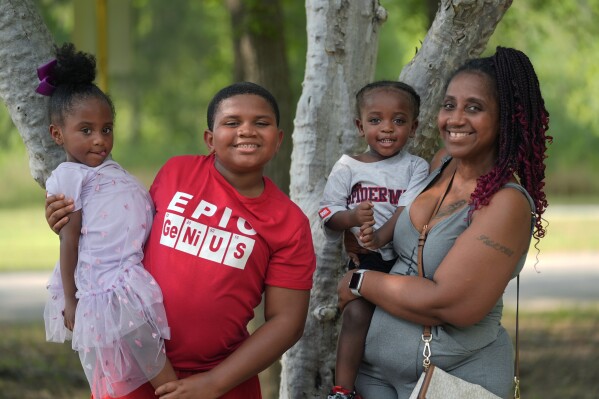 Tamika Davis, right, poses with three of her children, from left, Shanara, 3, Matthew, 11, and Lionel Jr., 2, at MLK Park in San Antonio, Thursday, May 30, 2024. Davis said friends and family watched her kids for most of her doctor visits during treatment last year for colon cancer. But she couldn't afford additional childcare, and she didn't know where to look for assistance. (AP Photo/Eric Gay)