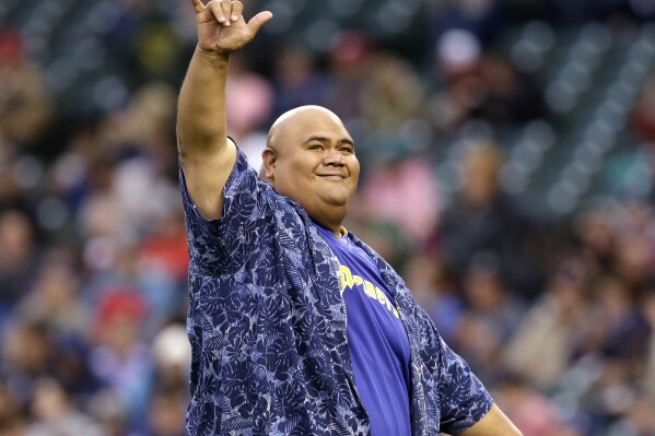 FILE - Actor Taylor Wily, also known as Teila Tuli, gestures to fans after throwing out the ceremonial first pitch before a baseball game between the Seattle Mariners and Texas Rangers in Seattle on June 14, 2014. Wily, an actor known for his roles on “Hawaii Five-0” and “Magnum P.I,” has died at 56. (AP Photo/Elaine Thompson, File)