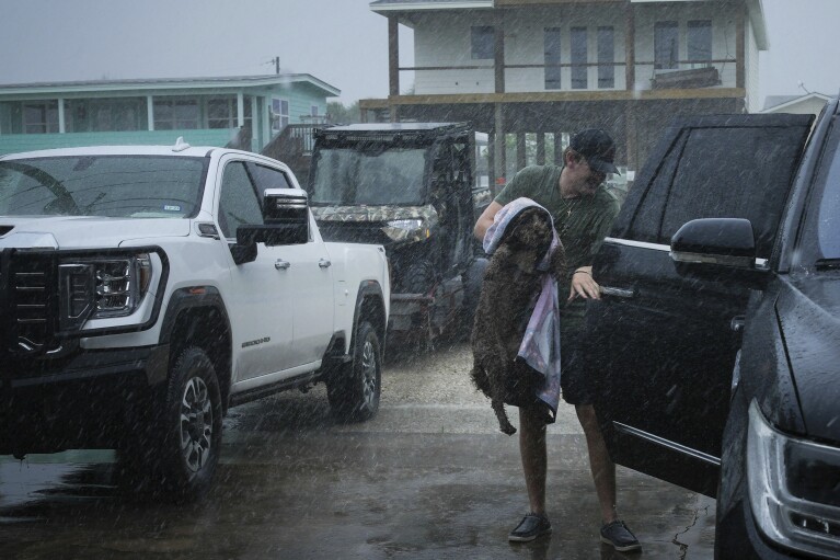 Blake Braun loads his dog Dolly into his family's vehicle as outer bands from Tropical Storm Beryl begin to hit the coast Sunday, July 7, 2024, in Port O'Connor, Texas. (Jon Shapley/Houston Chronicle via AP)