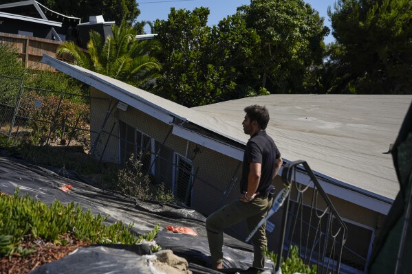 A reporter stands near a home that collapsed due to ongoing landslides in Rancho Palos Verdes, Calif., Tuesday, Sept. 3, 2024. (AP Photo/Jae C. Hong)