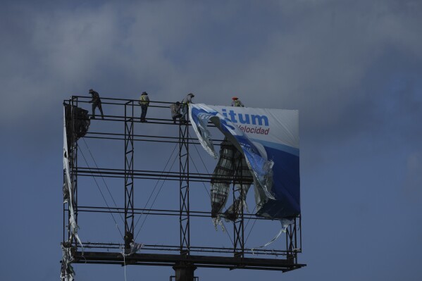 Workers remove an advertisement from a billboard for protection ahead of Hurricane Beryl's expected arrival, in Playa del Carmen, Mexico, Wednesday, July 3, 2024. (AP Photo/Fernando Llano)