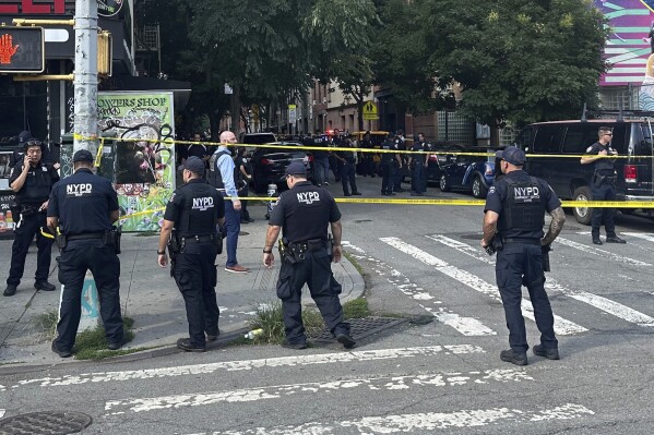 New York City Police Department officers secure the area where two police officers were shot, Thursday, Aug. 1, 2024. The officers were responding to a robbery call in Lower Manhattan in an area lined with shops, restaurants and street vendors. Witnesses said the officers were shot while chasing a fleeing suspect. (AP Photo/Jake Offenhartz)