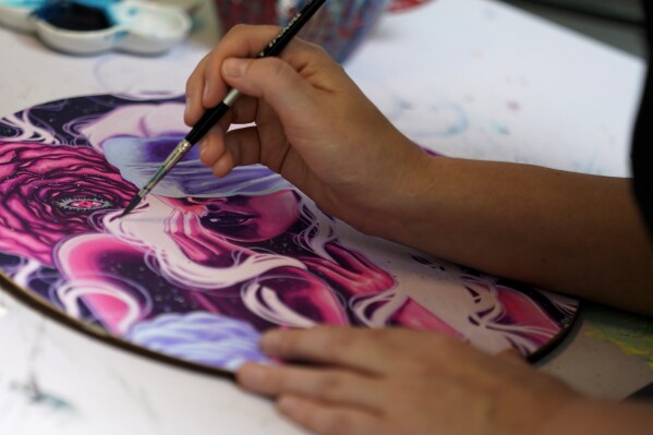 Artist Kelly McKernan paints in their studio Tuesday, Aug. 15, 2023, in Nashville, Tenn. McKernan is an artist and one of three plaintiffs in a lawsuit against artificial intelligence companies they allege have infringed on their copyright. (AP Photo/George Walker IV)