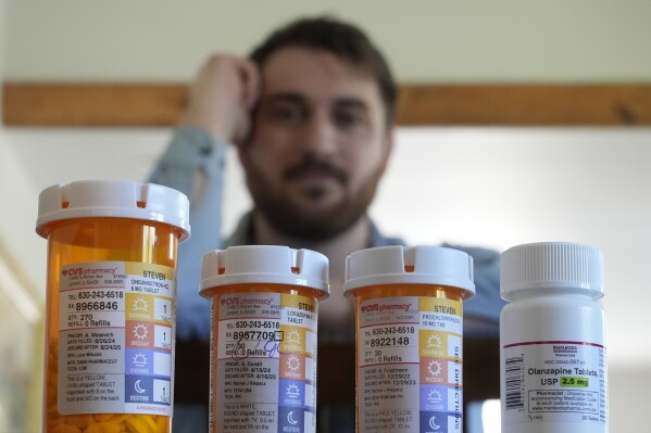 Cancer patient Steven Manetta sits for a portrait Monday, Sept. 9, 2024, in his Lemont, Ill., home with four of the five medicines he takes daily to battle the nausea from his chemotherapy. (AP Photo/Charles Rex Arbogast)