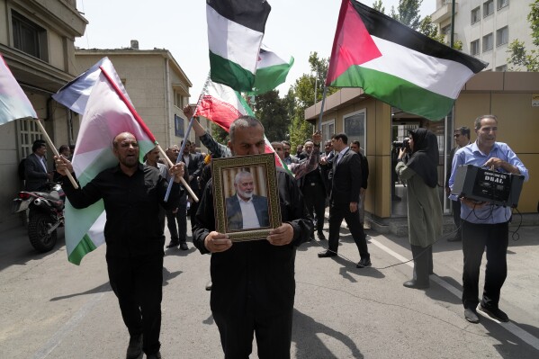 Members of Tehran University Council attend a protest to condemn the killing of Hamas political chief Ismail Haniyeh, shown in the picture at center, as they carry Iranian and Palestinian flags at the University in Tehran, Iran, Wednesday, July 31, 2024. Haniyeh, Hamas' political chief in exile who landed on Israel's hit list after the militant group staged its surprise Oct. 7 attacks, was killed in an airstrike in the Iranian capital early Wednesday. (AP Photo/Vahid Salemi)