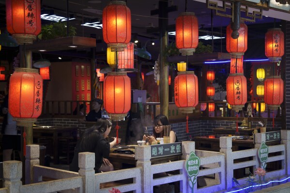 People have dinner behind Chinese lantern displayed at a restaurant in Beijing, China, Tuesday, July 9, 2024. (AP Photo/Vincent Thian)