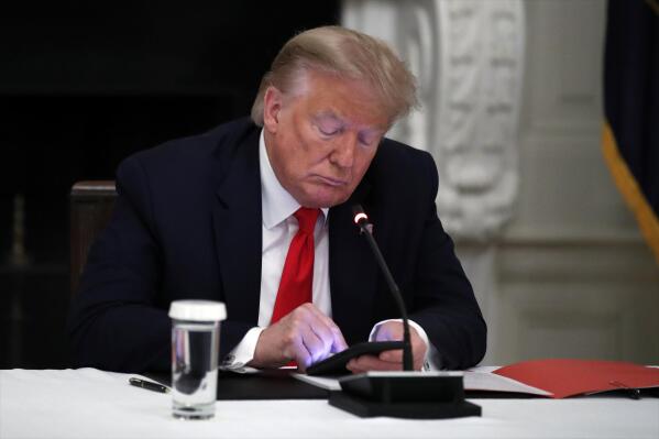 FILE - In this Thursday, June 18, 2020 file photo, President Donald Trump looks at his phone during a roundtable with governors on the reopening of America's small businesses, in the State Dining Room of the White House in Washington. On Wednesday, Jan. 25, 2023, Facebook parent Meta said in a blog post it is reinstating former President Trump’s personal account after two-year suspension following the Jan. 6 insurrection. (AP Photo/Alex Brandon, File)