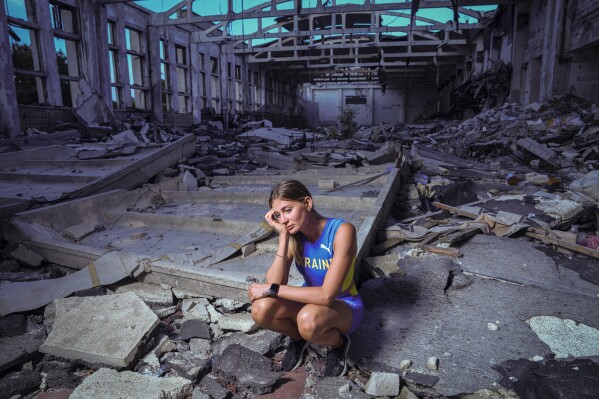 Kateryna Tabashnyk, a high jumper, sits for a portrait Sunday, June 9, 2024, at the athletics arena of the "Polytechnic" sports complex, which was destroyed by a Russian rocket attack, in Kharkiv, Ukraine. On the eve of the war, which started Feb. 24, 2022, Ukraine cancelled its athletics championship and Tabashnyk was in Kharkiv. The threat posed by thousands of Russian troops at the border, just 20 kilometers (12 miles) from her hometown, was real. But Tabashnyk said, “I was 100% sure that this could not happen.” (AP Photo/Evgeniy Maloletka)