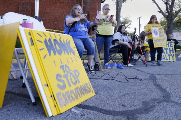 Dani Allen, center left with microphone, an anti-death penalty advocate, speaks during a protest outside the prison where Robert Roberson is scheduled for execution at the Huntsville Unit of the Texas State Penitentiary, Thursday, Oct. 17, 2024, in Huntsville, Texas. (AP Photo/Michael Wyke)