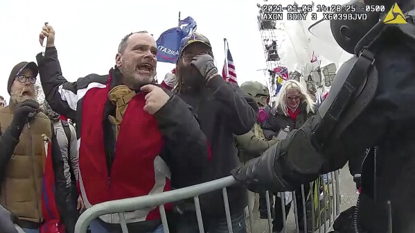 FILE- This still frame from Metropolitan Police Department body worn camera video shows Thomas Webster, in red jacket, at a barricade line at on the west front of the U.S. Capitol on Jan. 6, 2021, in Washington. A federal appeals court has upheld a retired New York Police Department officer’s conviction and 10-year prison sentence for assaulting a police officer during the Jan. 6, 2021, siege at the U.S. Capitol. A three-judge panel from the U.S. Court of Appeals for the District of Columbia Circuit on Tuesday rejected Thomas Webster’s claims that he was convicted by a biased jury. (Metropolitan Police Department via AP)