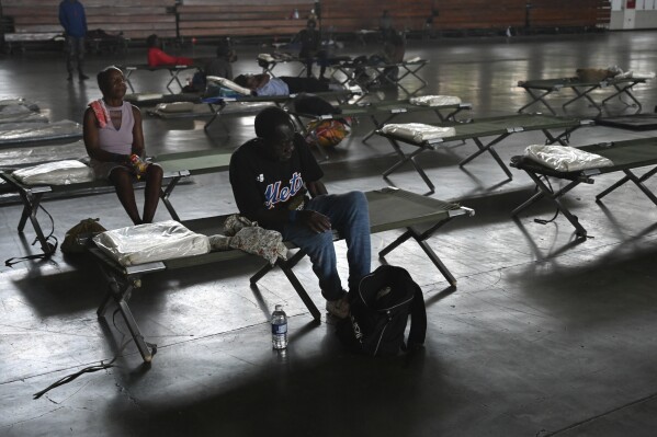 People sit on cots in the National Arena that has been transformed into a shelter in the aftermath of Hurricane Beryl, in Kingston, Jamaica, July 4, 2024. (AP Photo/Collin Reid)