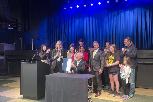 Minnesota Gov. Tim Walz beams while holding up the so-called Taylor Swift bill he signed into law as lawmakers, First Avenue employees and online ticket buyers clap Tuesday, May 7, 2024, inside the First Avenue concert venue in Minneapolis. The law, prompted by the frustration a legislator felt at not being able to buy tickets to Swift's 2023 concert in Minneapolis, will require ticket sellers to disclose all fees up front and prohibit resellers from selling more than one copy of a ticket for live events held in Minnesota, among other measures. (AP Photo/Trisha Ahmed)