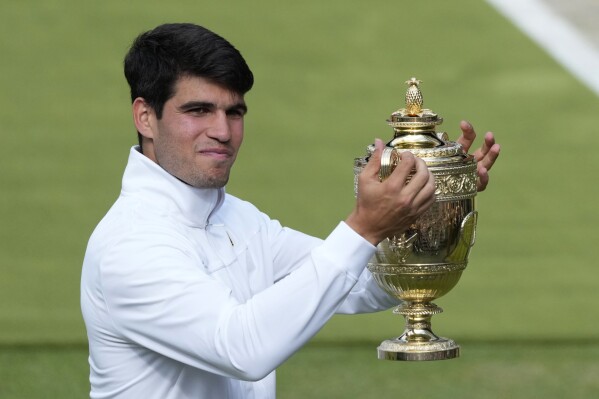 Carlos Alcaraz of Spain smiles as he holds up his trophy for the photographers after defeating Novak Djokovic of Serbia in the men's singles final at the Wimbledon tennis championships in London, Sunday, July 14, 2024. (AP Photo/Mosa'ab Elshamy)