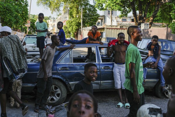 FILE - Youths hang out near cars serving as street barricades placed there by residents to deter gangs from entering their neighborhood, in downtown Port-au-Prince, Haiti, May 17, 2024. (AP Photo/Ramon Espinosa, File)