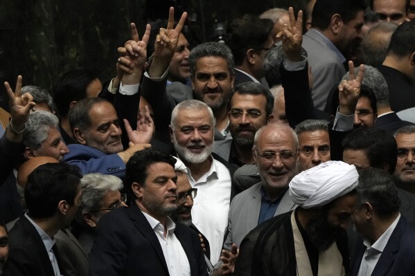 Palestinian Hamas chief Ismail Haniyeh, center, flashes a victory sign as he is surrounded by a group of Iranian lawmakers after the conclusion of the swearing-in ceremony of newly-elected Iranian President Masoud Pezeshkian at the parliament in Tehran, Iran, Tuesday, 30, 2024. (AP Photo/Vahid Salemi)