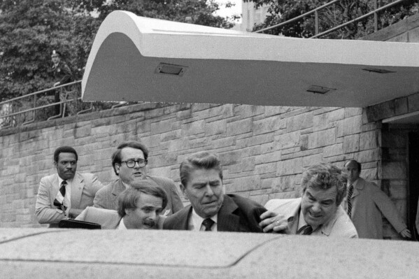 FILE - President Ronald Reagan waves and then looks up before being shoved into the President's limousine by secret service agents after being shot outside a Washington hotel, March 30, 1981. The assassination attempt of former President Donald Trump has parallels to the last time a president or presidential candidate was wounded — in 1981 when Ronald Reagan was nearly killed by an assailant's bullet. Reagan's life was spared thanks to the quick actions of a Secret Service agent and the skill of doctors and nurses at a Washington, D.C., hospital. (AP Photo/Ron Edmonds, File)